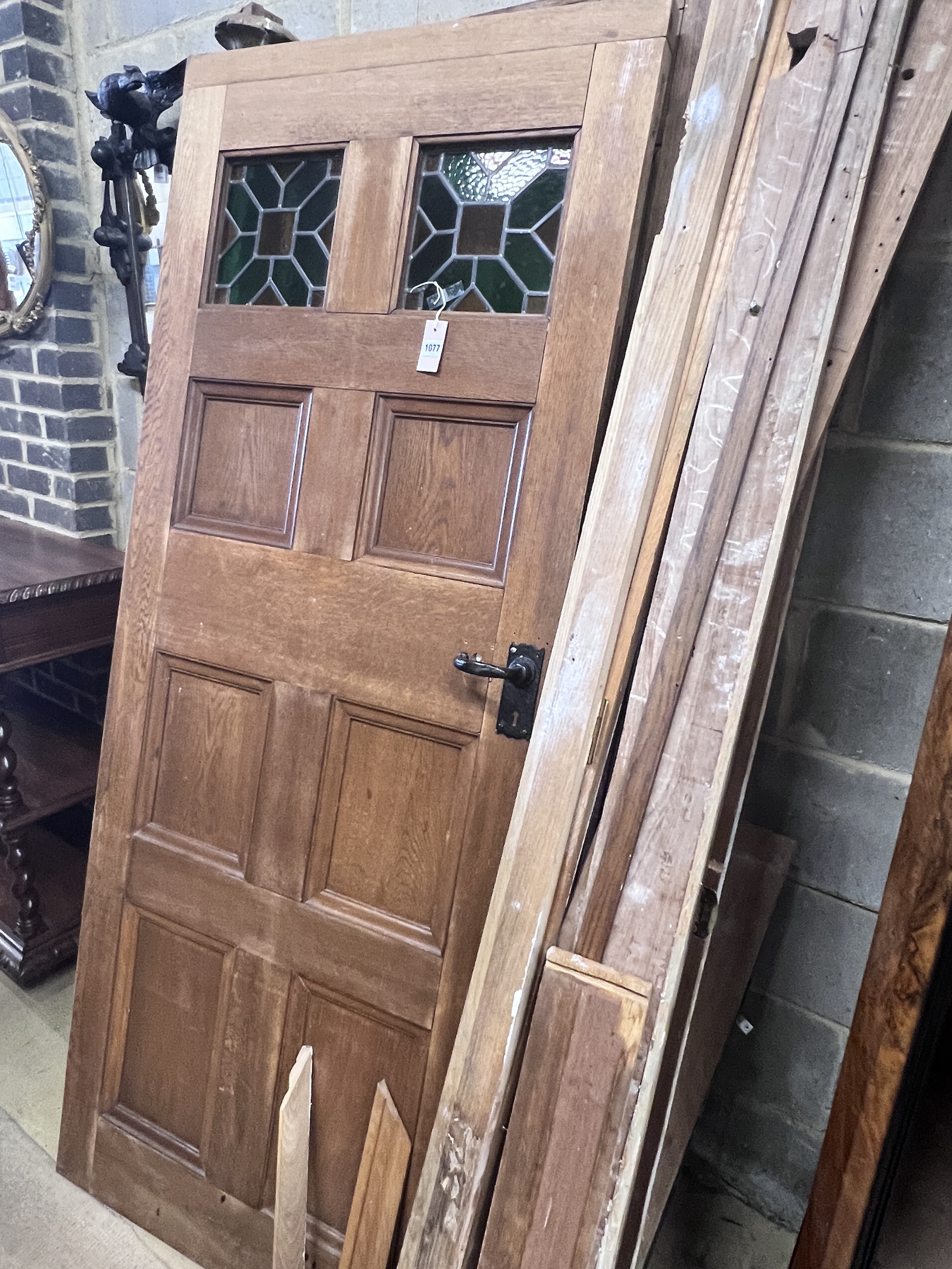 A panelled oak door with inset stained glass panels, width 78cm, height 194cm, another panelled door, sundry framework and assorted columns